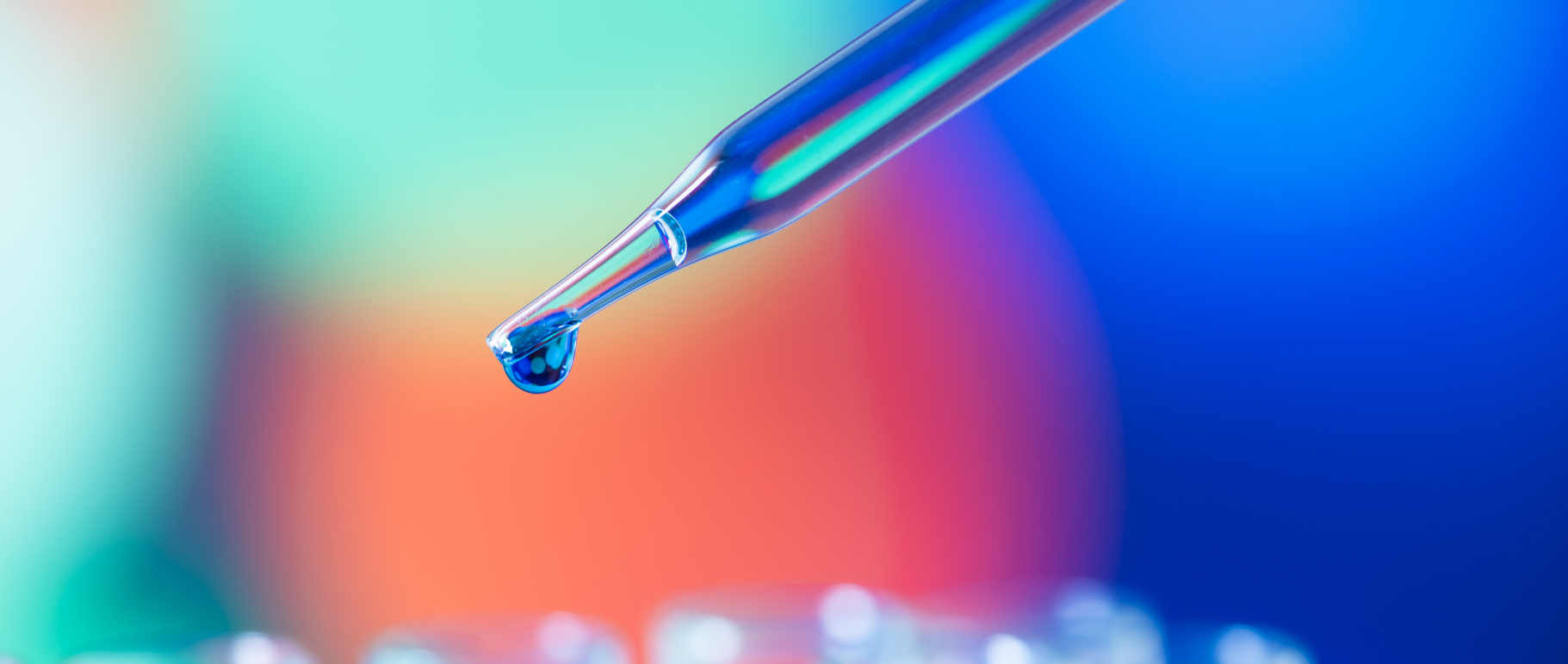 A pipette dripping some solution in front of a blurred background